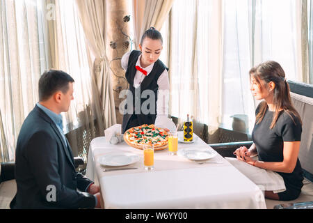 Le serveur met sur la table une pizza au restaurant. Banque D'Images