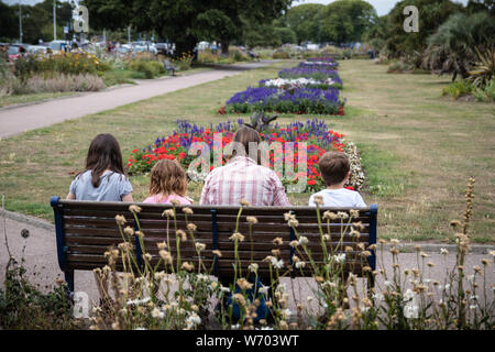 Une famille étaient assis ensemble sur un banc de parc au soleil Banque D'Images