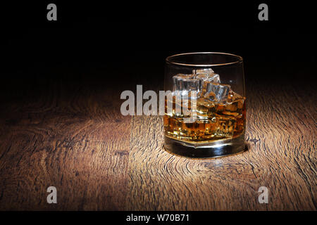 Un verre de scotch dans Tumbler avec de la glace à la surface des roches sur le vieux bois Banque D'Images