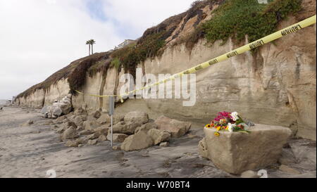 Ruban de signalisation et d'avertissement à la plage de rochers instables Grandview, à Encinitas - site d'un bluff mortel s'effondrer. Fleurs pleurent la mort de la plage. Banque D'Images