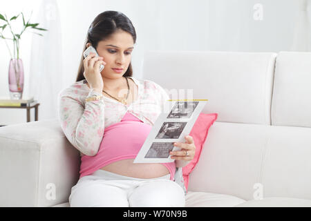 Pregnant Woman talking on mobile phone et holding rapport échographie Banque D'Images