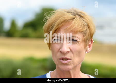 Femme à la recherche de ses lèvres alors qu'elle a l'air de côté avec un froncement de concentration dans un close up head shot en plein air dans la campagne Banque D'Images