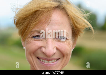 Femme heureuse avec un beau sourire plein de vivacité et moderne rouge court cheveux blonds dans un close up head shot en plein air dans la campagne Banque D'Images