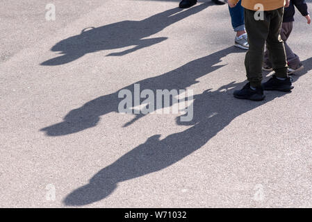 Ombres et silhouettes de trois enfants jouant dans une rue sur la surface de la route d'asphalte comme arrière-plan ou de texture Banque D'Images