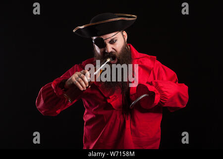 Portrait d'homme barbu habillé comme un pirate pour Halloween. Pirate à l'ouverture de la bouteille avec sa bouche. Banque D'Images