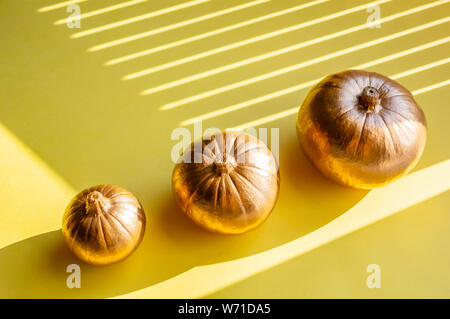 Trois citrouilles décoratives dorées sur un fond jaune. Halloween concept. Les ombres dures, plein soleil. Close-up Banque D'Images