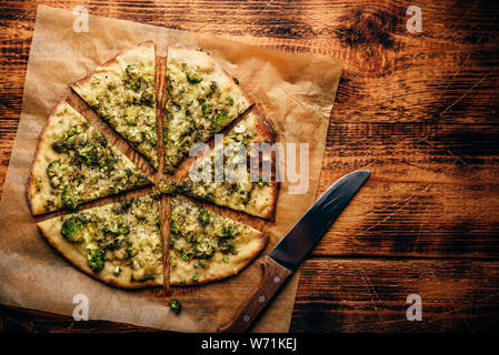 Tranches de pizza italienne avec brocoli, sauce pesto, épices et fromage sur du papier sulfurisé sur table en bois rustique. Vue de dessus Banque D'Images