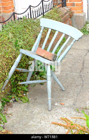 West Sussex, Angleterre, Royaume-Uni. Une chaise en bois peint avec une maison brique sur top abandonné dans un jardin à l'avant. Banque D'Images