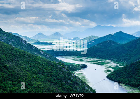 Le Monténégro, montagnes boisées entourant l'eau qui coule à travers la rivière crnojevica Valley dans le lac de Skadar avec des bateaux d'excursion Banque D'Images