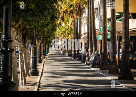 21 novembre 2017 - Marbella, Espagne. Les touristes à l'extérieur le front de cafés avec des palmiers et du soleil Banque D'Images