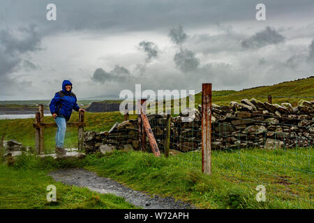 Femme sautant une clôture sur la promenade côtière de Doolin route vers les falaises de Moher, géoparc géosites et sauvage de l'Atlantique, Chemin, jour de pluie de printemps Banque D'Images