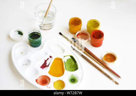 Gouache multi-couleur des peintures, pinceaux, palette et un verre d'eau pour les pinceaux sur un fond blanc Banque D'Images