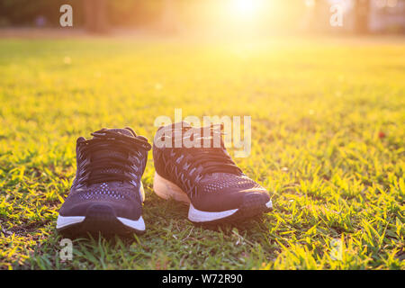 Près de nouvelles paires de chaussures de course noir / chaussures sneaker sur champ d'herbe verte dans le parc à l'heure du coucher du soleil. Ton ver, la lumière du soleil et l'effet lens flare w Banque D'Images