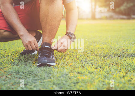 Close up man lier corde sur sa chaussure de sport. Préparation de l'exécution dans le parc au coucher du soleil. L'exercice et une saine utilisation concept Banque D'Images