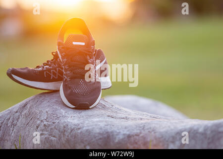 Près de nouvelles paires de chaussures de course noir / chaussures sneaker sur champ d'herbe verte dans le parc à l'heure du coucher du soleil. Ton ver, la lumière du soleil et l'effet lens flare w Banque D'Images