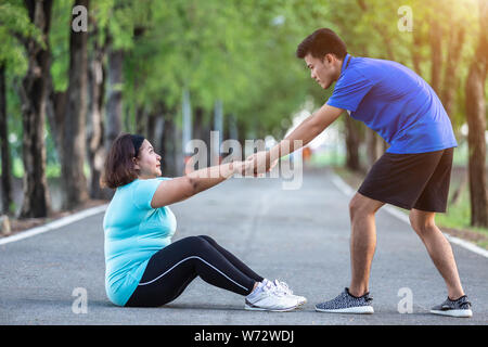 L'homme asiatique tirant la main et donner de l'encouragement à la grosse femme qui fatigué et assis sur sol Banque D'Images