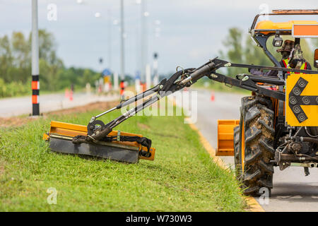 Tracteur avec une tondeuse mécanique de la tonte du gazon sur le côté de la route asphaltée. Concept de plein air de travail Banque D'Images