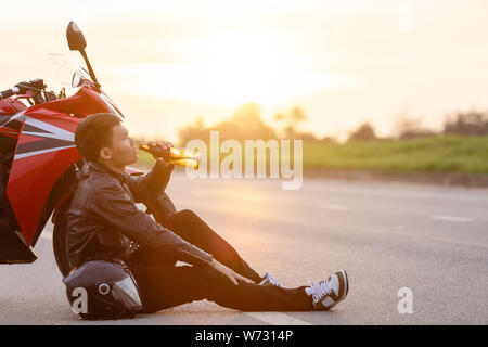 Motocycliste assis sur la route à côté de sa moto et de boire une bière ou d'alcool. Safe ride concept Banque D'Images