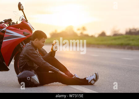 Motocycliste assis sur la route à côté de sa moto et de boire une bière ou d'alcool. Safe ride concept Banque D'Images