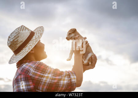 Les jeunes agriculteurs d'Asie en jouant avec son petit brun chiot dans la soirée après le travail. Happy farm concept Banque D'Images