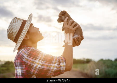 Les jeunes agriculteurs d'Asie en jouant avec son petit brun chiot dans la soirée après le travail. Happy farm concept Banque D'Images