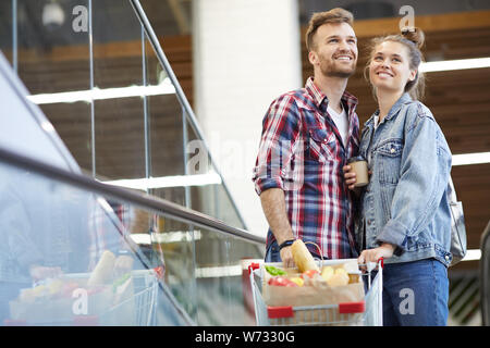 Portrait of young couple riding contemporain dans l'escalator et centre commercial shopping avec des provisions , copy space Banque D'Images