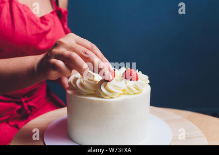 Décorées avec des baies d'une pâtisserie gâteau biscuit avec crème blanche. Cake se dresse sur une table en bois. Le concept de pâtisserie maison, la cuisson des gâteaux. Banque D'Images