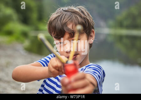 Bully blanc garçon de 8 ans joue avec slingshot en parc et la préparation de tir. Banque D'Images