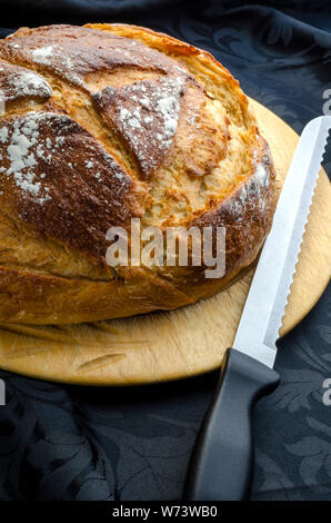 Une miche de pain au levain du pain et debout sur un bord à l'aide d'un couteau prêt à être découpé et mangé. Banque D'Images