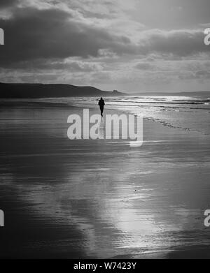 La Solitude:Une silhouette d'une personne marchant le long d'une plage déserte sur un matin d'hiver. L'image en noir et blanc met en lumière les réflexions & scene. Banque D'Images