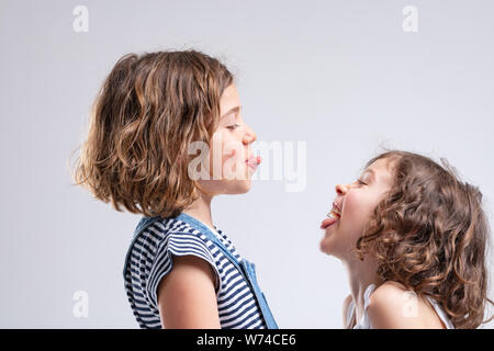 Deux jeunes filles espiègles coquines sortent leur langue à l'autre tout en se tenant face à face isolated on white Banque D'Images