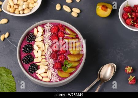 Smoothie déjeuner sain bol avec les mûres, les prunes, les framboises, les arachides et les graines de sésame sur un fond sombre, photo horizontale Banque D'Images