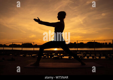 Woman practicing yoga dans le coucher du soleil. Virabhadrasana / Warrior pose Banque D'Images