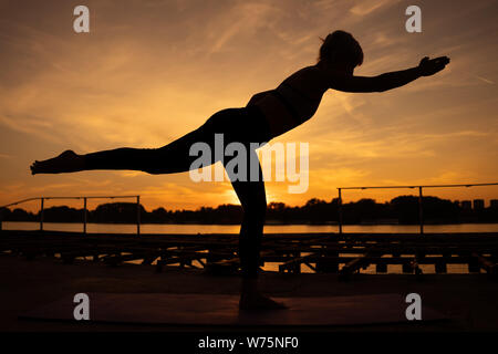 Woman practicing yoga dans le coucher du soleil. Virabhadrasana / Warrior pose Banque D'Images