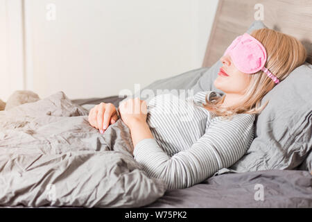 Young blonde woman sleeping in bed. Libre passage portrait de belles femmes portant des pyjamas rayés en appui sur le lit confortable, allongé sur gris pi Banque D'Images