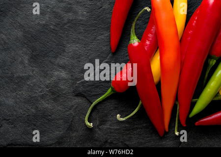 Tas de mélange rouge, jaune, orange et vert piments de cayenne isolé sur l'ardoise noire à partir de ci-dessus. L'espace pour le texte. Banque D'Images