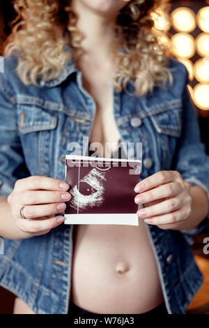 Les jeunes femmes enceintes belle blonde modèle mode femme veste en jean en studio en holding test aux ultrasons et attendre bébé, Close up of test aux ultrasons Banque D'Images