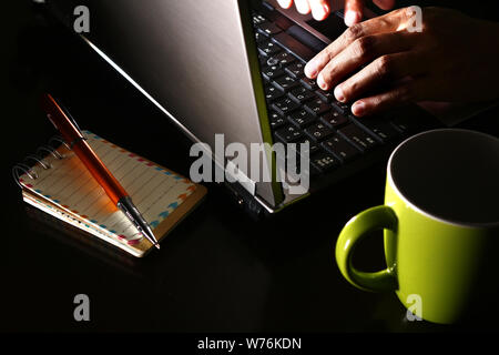 Photo d'une main sur un ordinateur portable, une tasse de café, un ordinateur portable et stylo-bille Banque D'Images