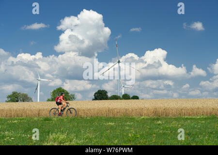 Nice, femme active, école son vtt électrique entre champs de blé et le vent wheewls d'un parc éolien sur le Jura souabe près de la ville d'Aalen, Banque D'Images