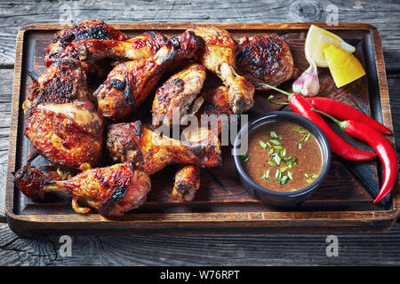 Poulet Jerk jamaïcain grillé chaud sur un board avec la sauce citron et sur une table en bois rustique, vue horizontale à partir de ci-dessus, close-up Banque D'Images