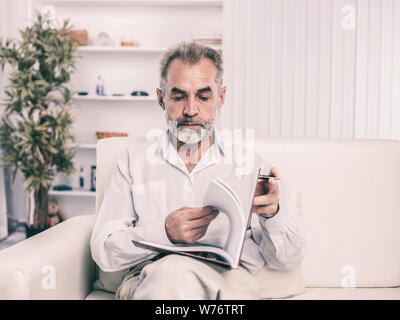 Homme d'affaires réussi avec stylet et business magazine, assis sur une chaise le bureau moderne Banque D'Images