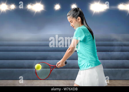 Femme Asiatique avec une raquette de tennis dans ses mains frapper la balle sur le court intérieur Banque D'Images