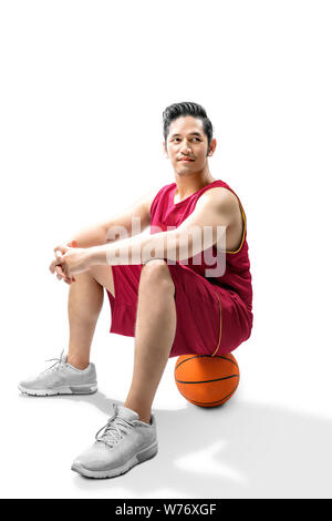 Joueur de basket-ball homme asiatique assis sur la balle plus isolé sur fond blanc Banque D'Images