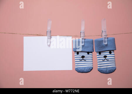 Chaussettes bébé mignon avec un visage et carte vierge accroché sur une corde à linge Banque D'Images