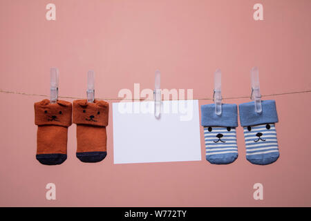 Chaussettes bébé mignon avec un visage et carte vierge accroché sur une corde à linge Banque D'Images