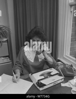 Années 1980, secrétaire de bureau au téléphone, stylo à la main, avec journal intime et machine à écrire de l'époque sur son bureau, Angleterre, Royaume-Uni. Banque D'Images