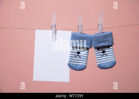 Chaussettes bébé mignon avec un visage et carte vierge accroché sur une corde à linge Banque D'Images