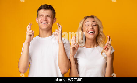 Young man and woman crossing fingers avec espoir aux yeux clos Banque D'Images