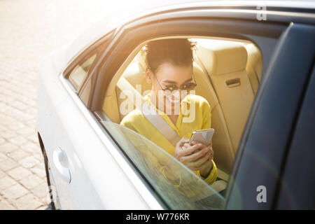 African-American girl texting on phone, sitting in car Banque D'Images