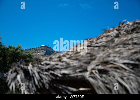 La paille d'un parasol, d'un arbre et le monastère du prophète Elias au sommet Le sommet le plus élevé de Santorin, le mont Profitis Ilias Banque D'Images